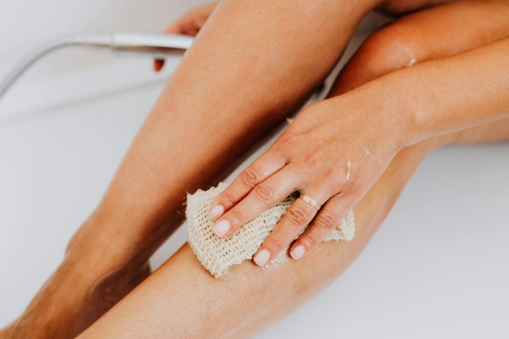 person using loofah body scrub sponge on leg
